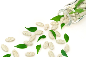Herbal supplement pills and fresh leaves spilling out of bottle  alternative medicine concept